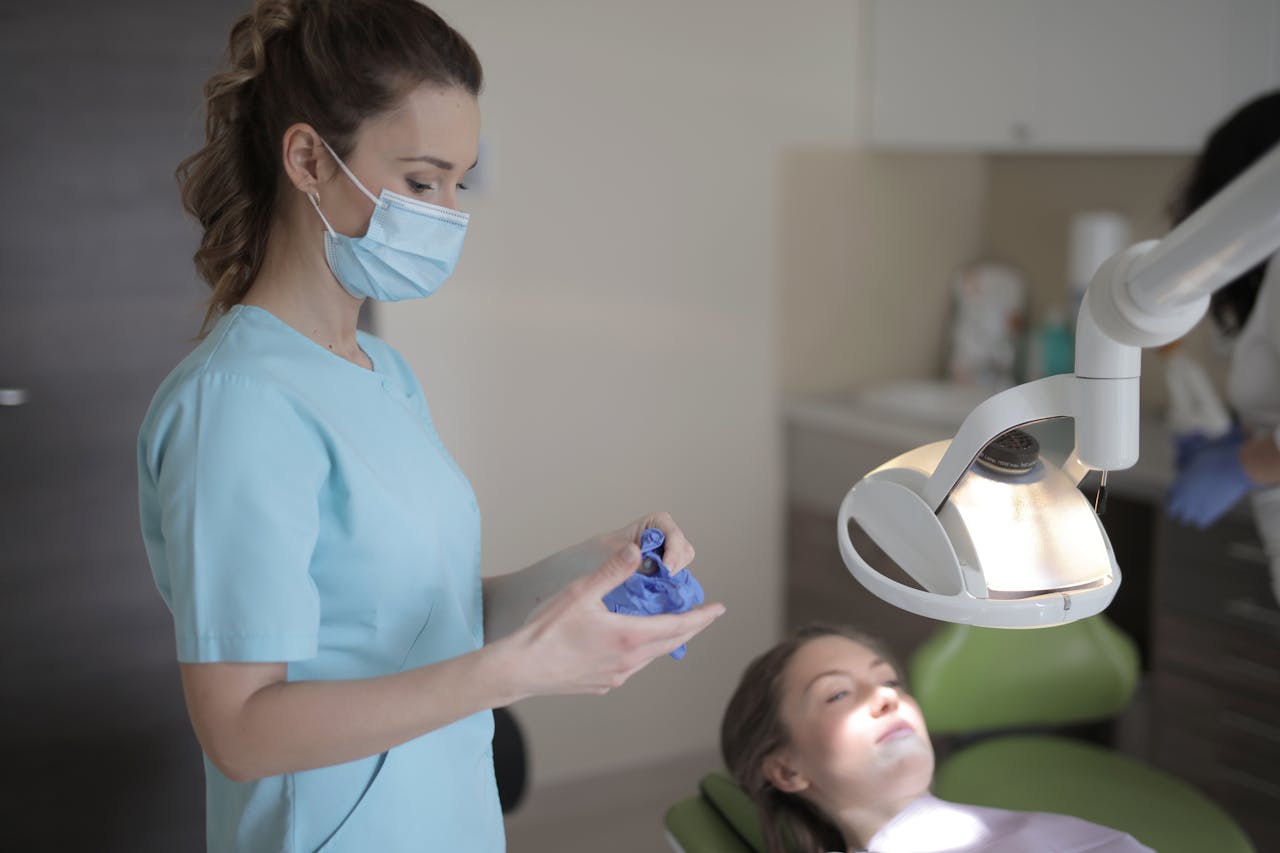 Female dentist preparing gloves in a dental clinic with patient ready for examination.